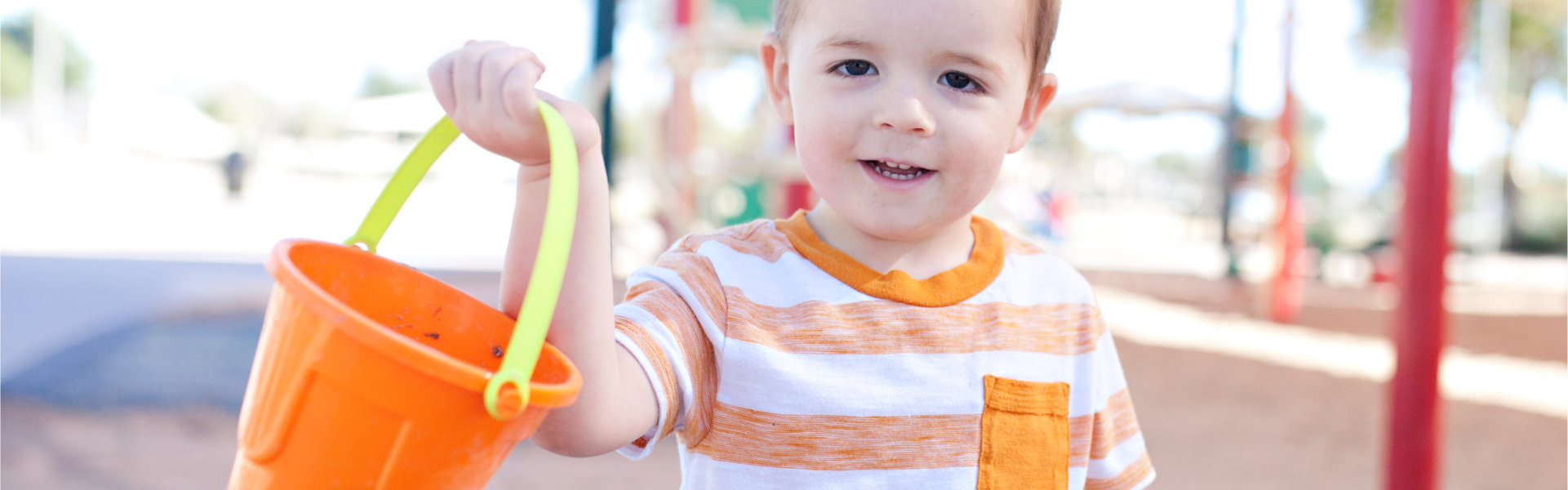 Child in a playground with a small bucket.