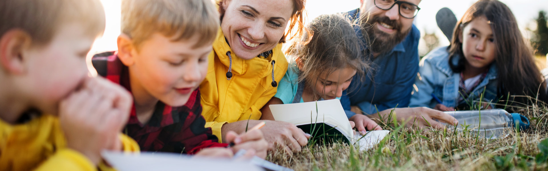 Educators lying on grass with children reading books.